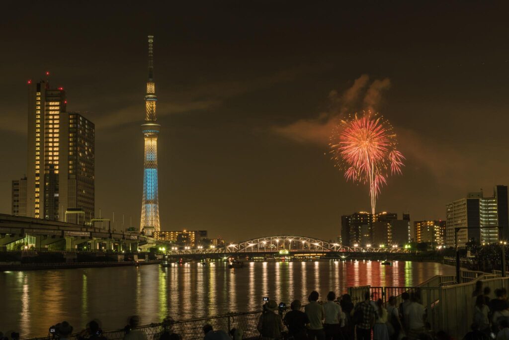 Suasana festival kembang api Jepang 2026 di Tokyo dengan langit malam penuh warna dan penonton mengenakan yukata